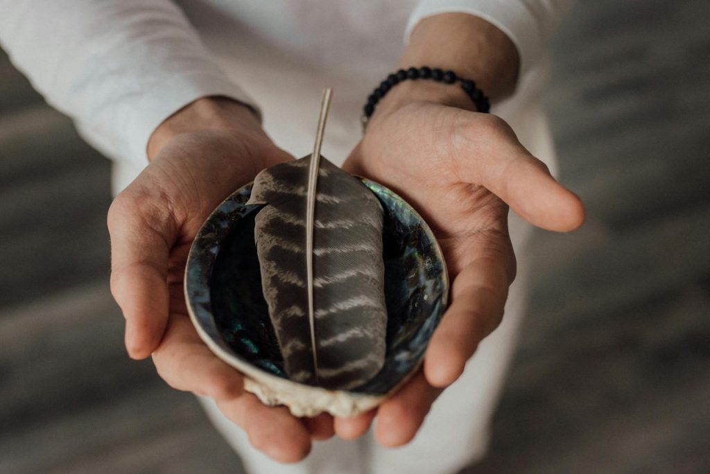 Close-up of hands cradling a feather in a decorative bowl, symbolizing tranquility.